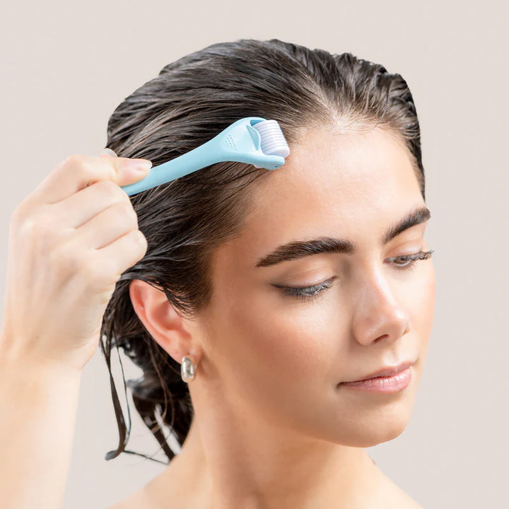 Woman using a Derma Scalp Roller on her wet hair against a neutral background